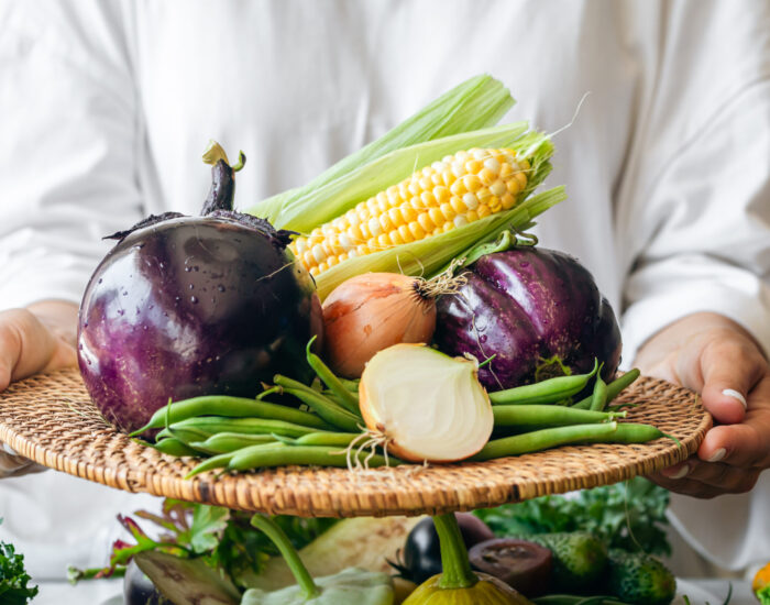 A woman holds a plate with eggplant, onion, corn and green beans, close-up. A woman holds a plate with eggplant, onion, corn and green beans, close-up, healthy food preparation.